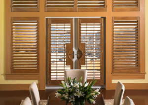 Beautiful set of wooden interior shutters as centerpiece in a wall of windows that also has wooden blinds 