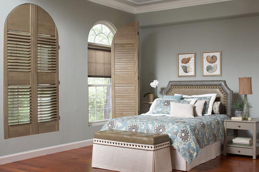 Wood shutters matching to a bedspread and paired with shades