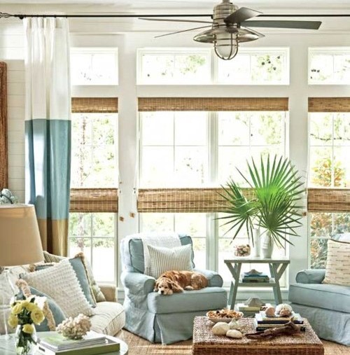 Woven wood shades with beach style draperies in a beach styled living room full of sandy cream colors and light blues.