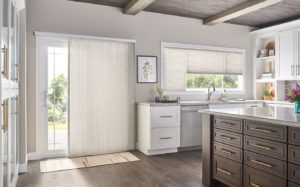View of a kitchen with vertical cellular shades on a patio door plus horizontal cellular shades on a window over the sink