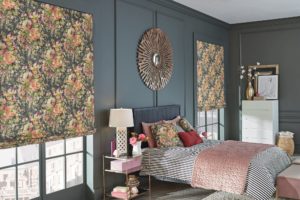 Bedroom with dark blue-green walls and floral-pattern shades that match throw covers on the bed