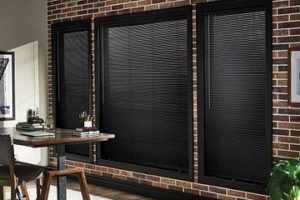 Black horizontal blinds over windows set in brick wall with brown wood table and chair 