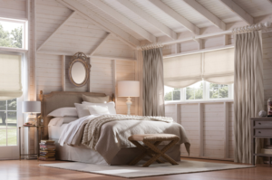 Rustic style bedroom with beams and sloping ceiling and wide but short window covered with lightweight shades and long curtains to give the impression of more height