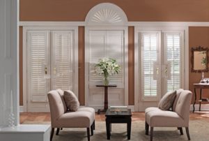 Luxury seating area with narrow white wood shutters on two sets of patio doors, a front door, and a custom shutter shading a round-top transom 