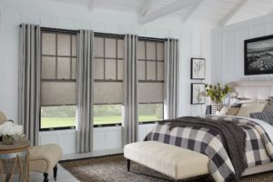 Luxury bedroom decorated in various shades of gray, brown, and black with four panels of beautiful, lined medium gray drapes adorning three black-frame windows with light brown shades