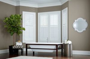 Four sets of white composite shutters on large bay window behind a soaking bathtub with taupe-and-white room decor. Example of custom window treatments adding home value.