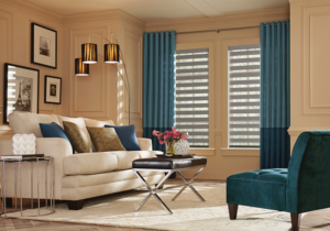 Deep blue drapes that transition to midnight blue, paired with gray silhouette blinds against tan walls in a seating area with off-white, matching blue, and earth colors - window treatment trends for 2023.